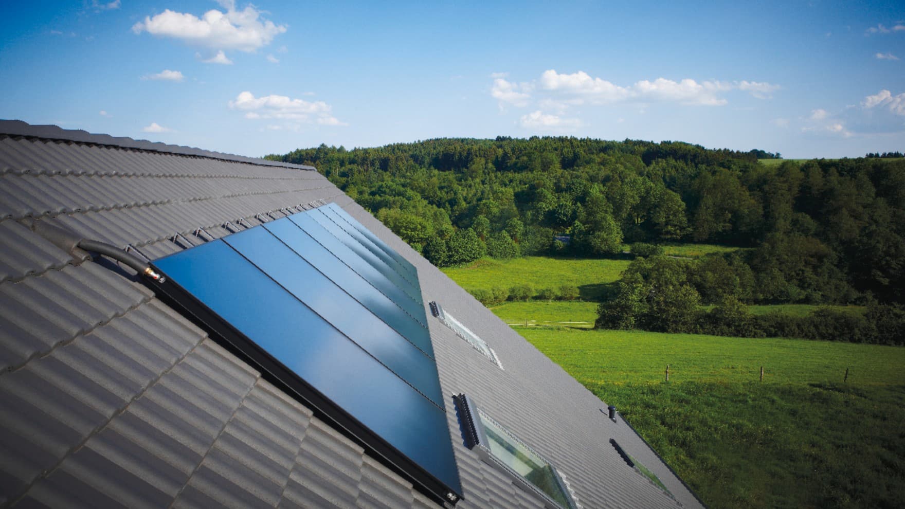 Vaillant Solarkollektoren auroTHERM plus auf dem Dach, im Hintergrund grüne Wiesen und Wälder bei strahlend blauem Sommerhimmel