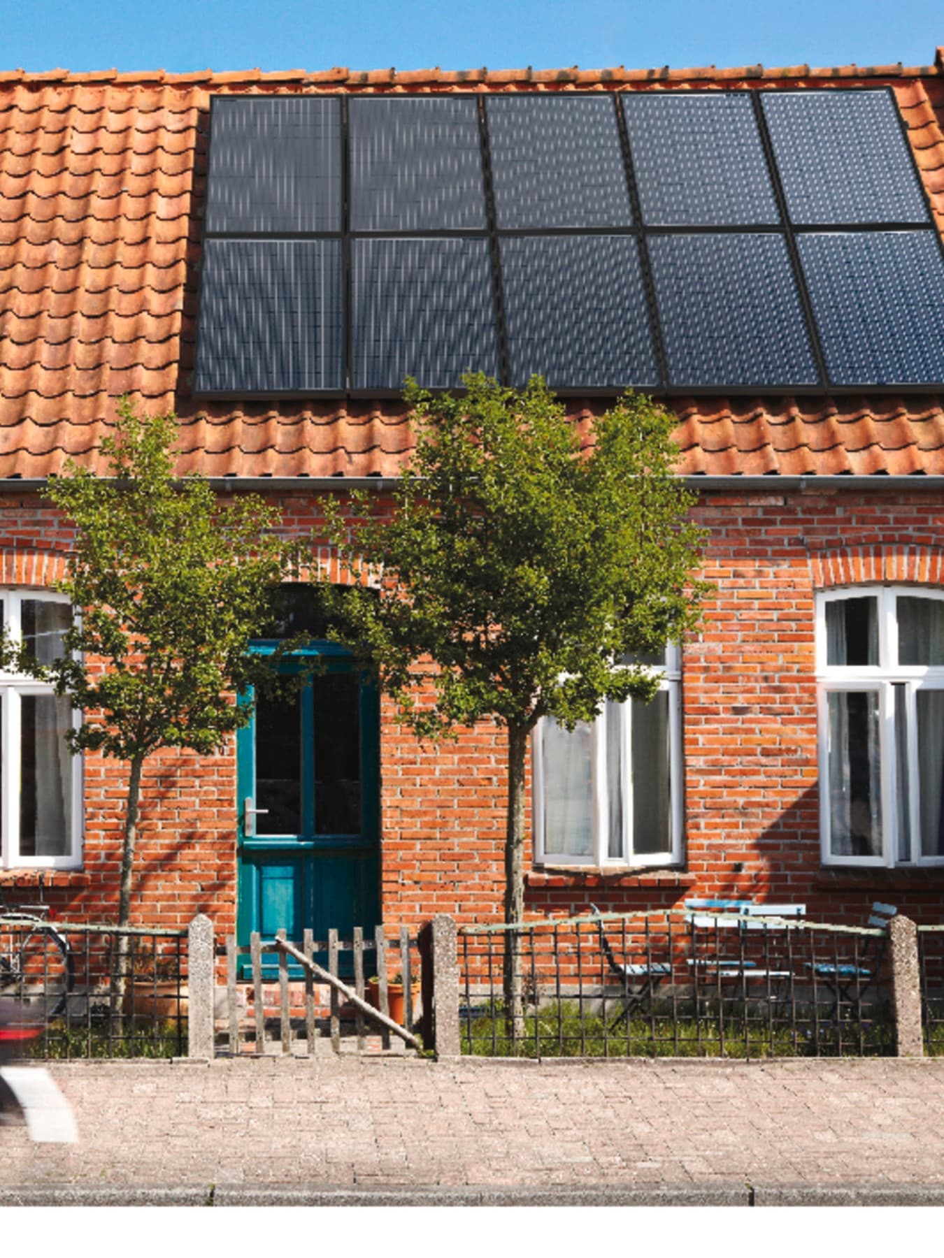Fahrradfahrer fährt an einem Backsteinhaus mit Solarpaneelen auf dem Dach vorbei.
