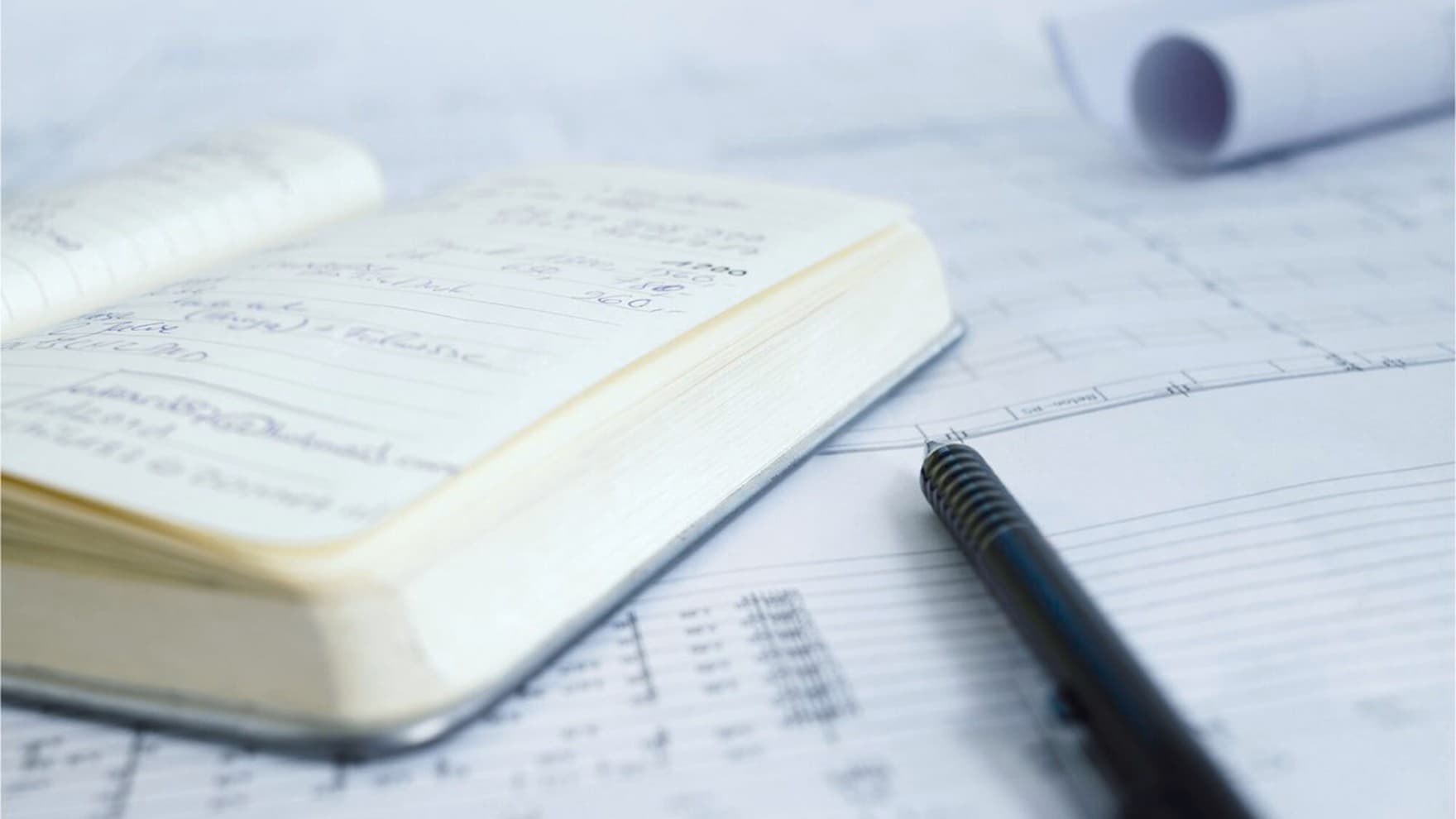 Ein Notizbuch und ein Stift liegen auf einem Dokument mit Zahlen und Tabellen.