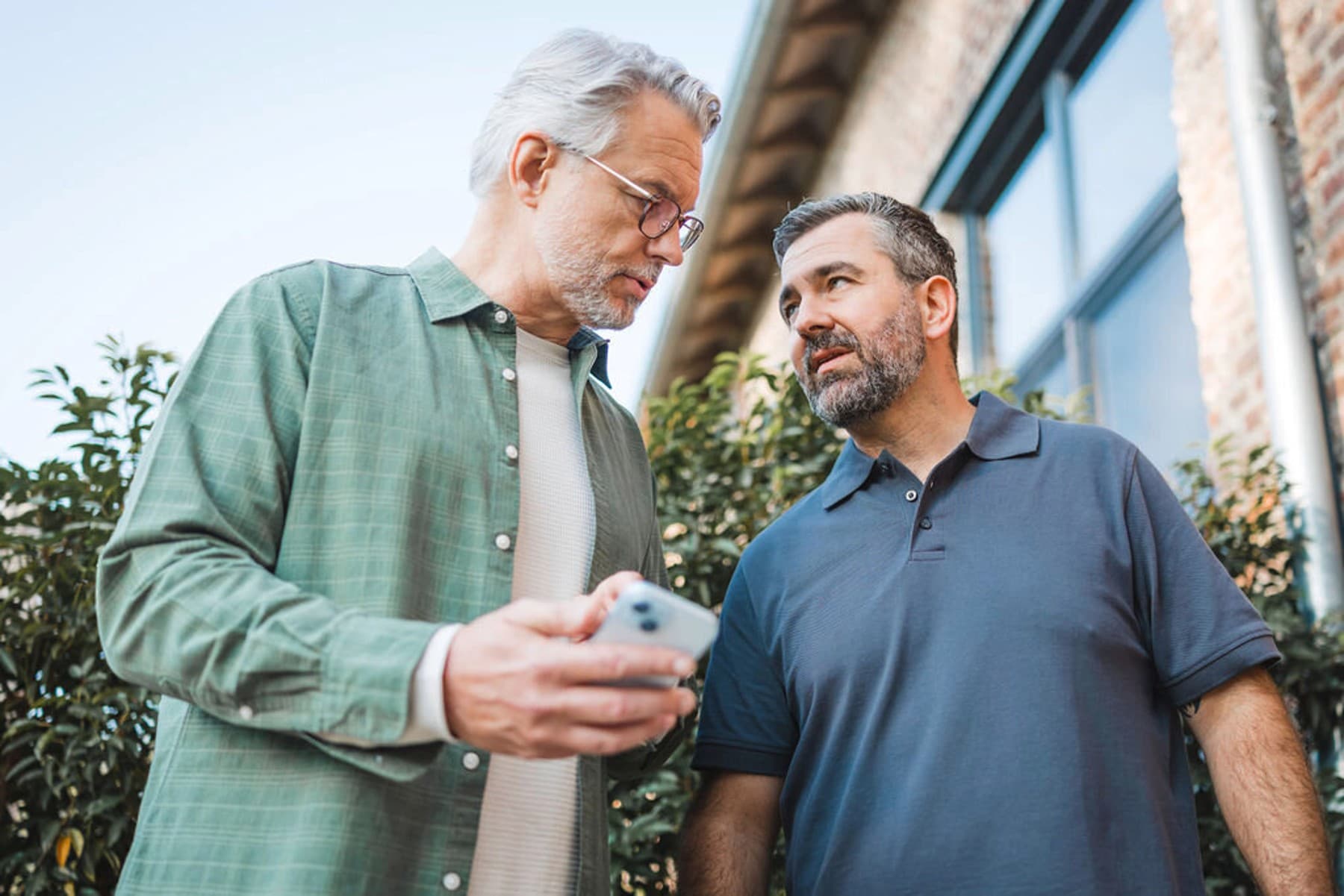 Zwei Männer, die vor einem Haus stehen mit einem Smartphone in der Hand.