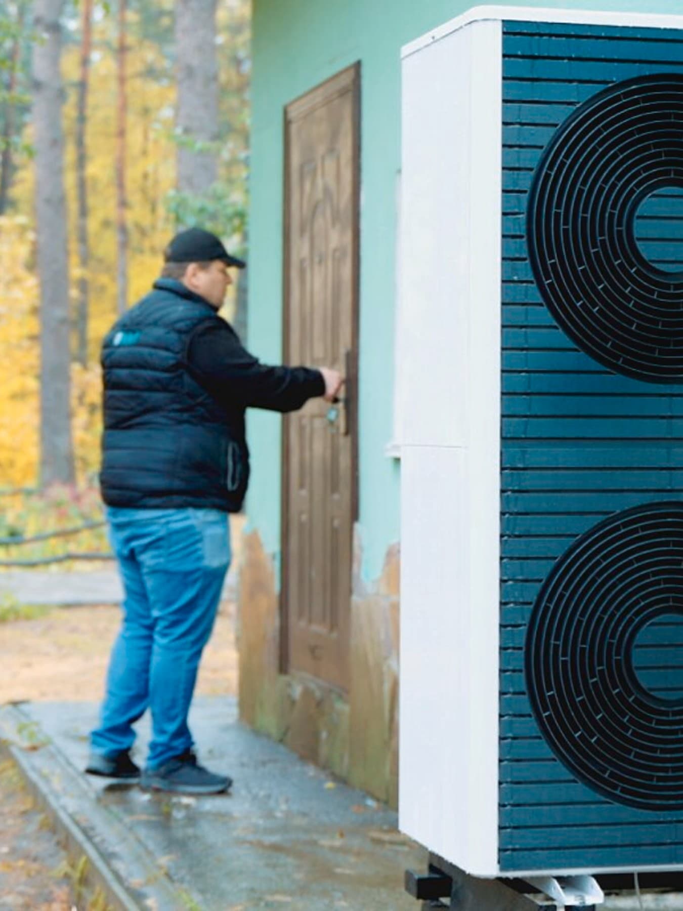 Eine Vaillant Wärmepumpe mit zwei Ventilatoren steht vor einem Haus im SOS Kinderdorf Brovary. Neben dem Haus ist ein Weg mit mehreren Bäumen, im Hintergrund steht ein Mann an der Tür des Hauses und hält seine Hand auf die Klinke.