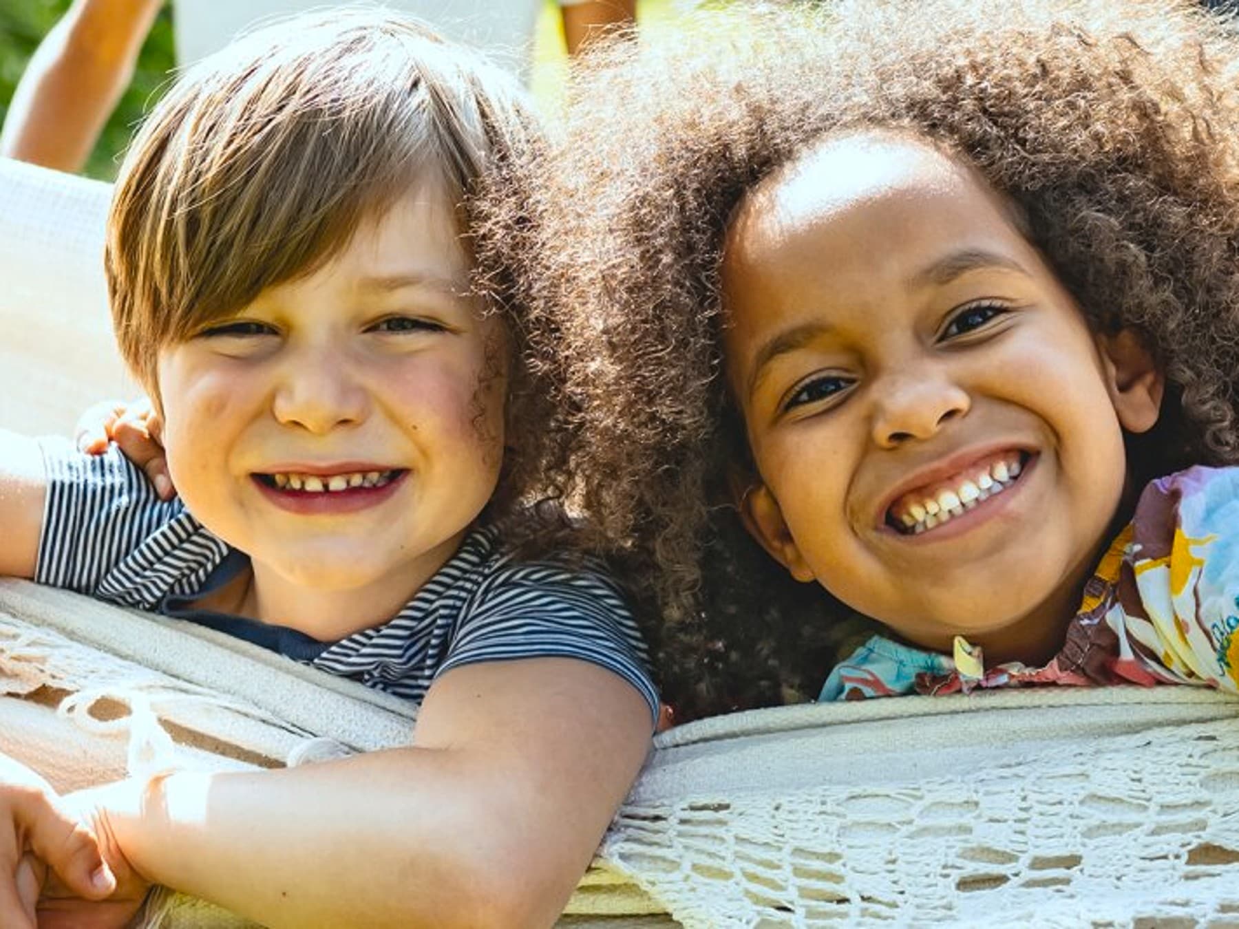 Zwei Kinder liegen lachend in einer Hängematte.