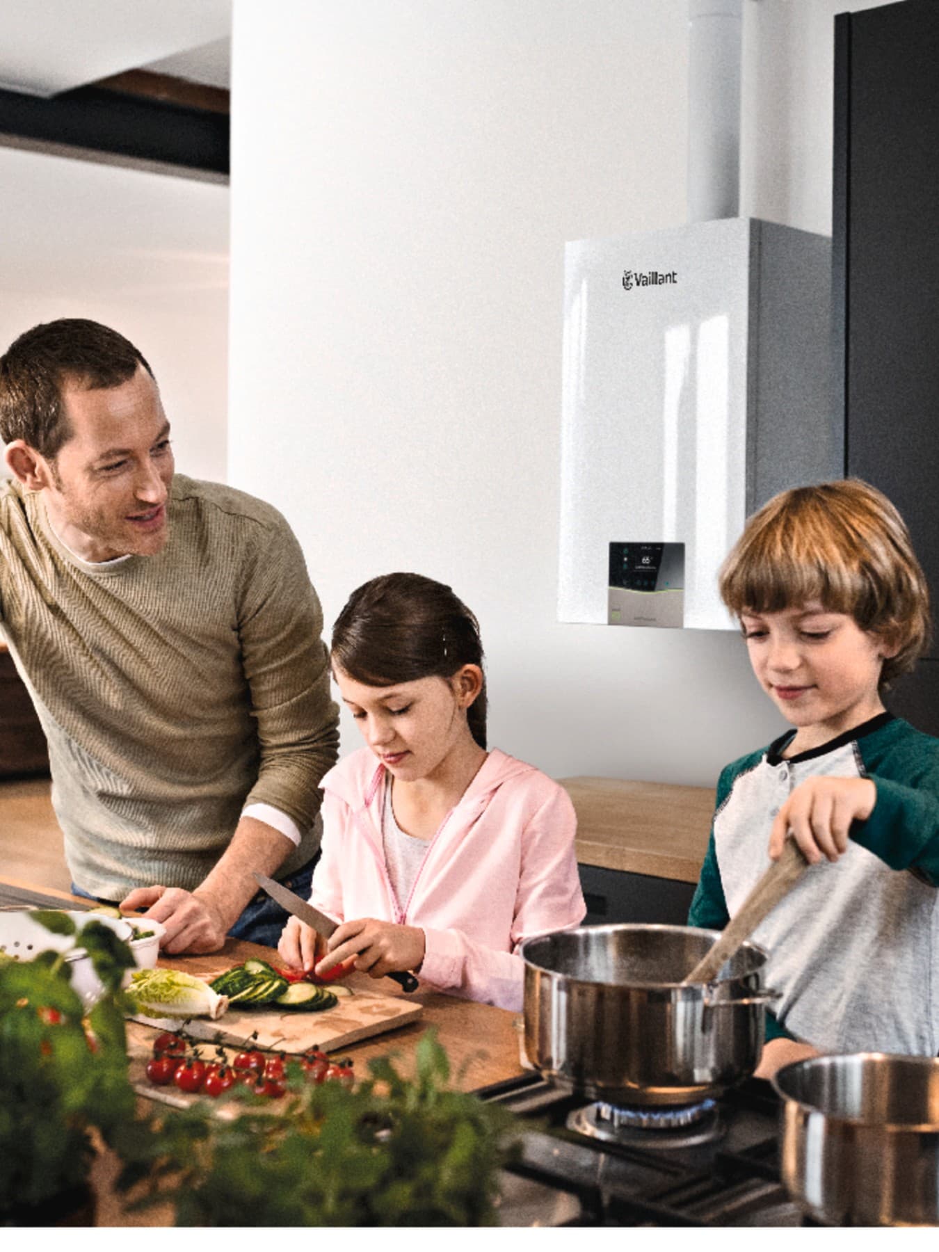 Vater und Kinder beim Kochen in der Küche. Im Hintergrund hängt ein Vaillant Gerät an der Wand