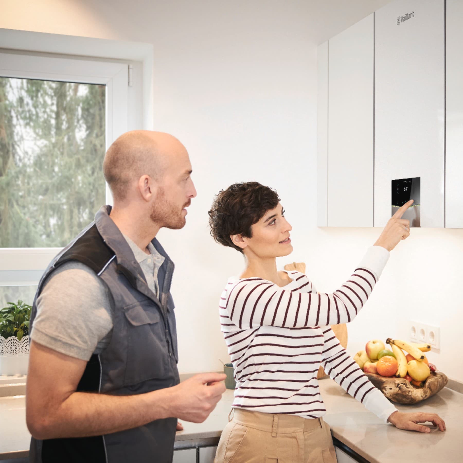 Fachhandwerker und Kundin stehen in der Küche. Die Kundin bedient das an der Wand hängende Gasgerät ecoTEC.