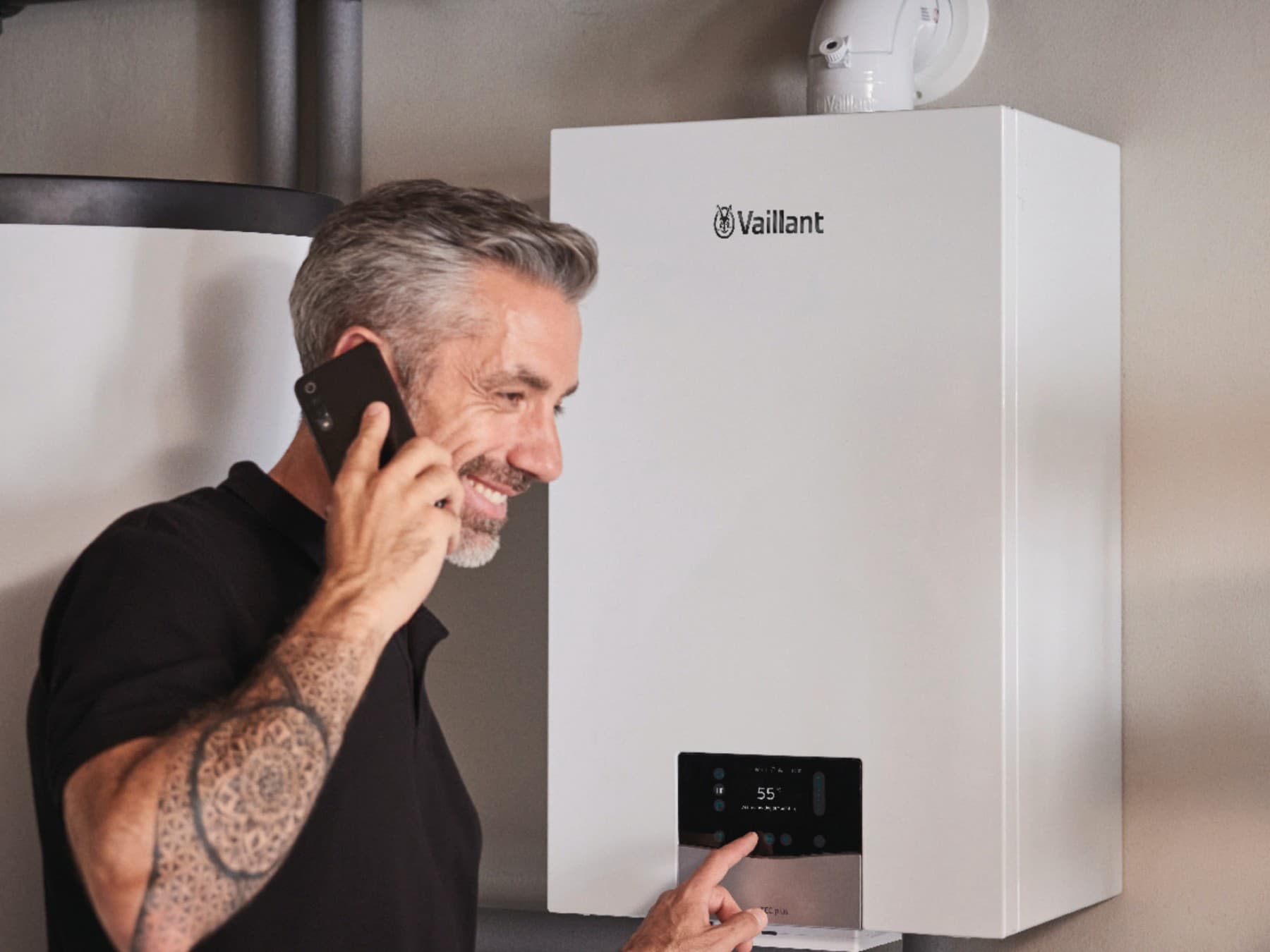 Eine Mann telefoniert und stellt etwas am Heizungsregler ein.